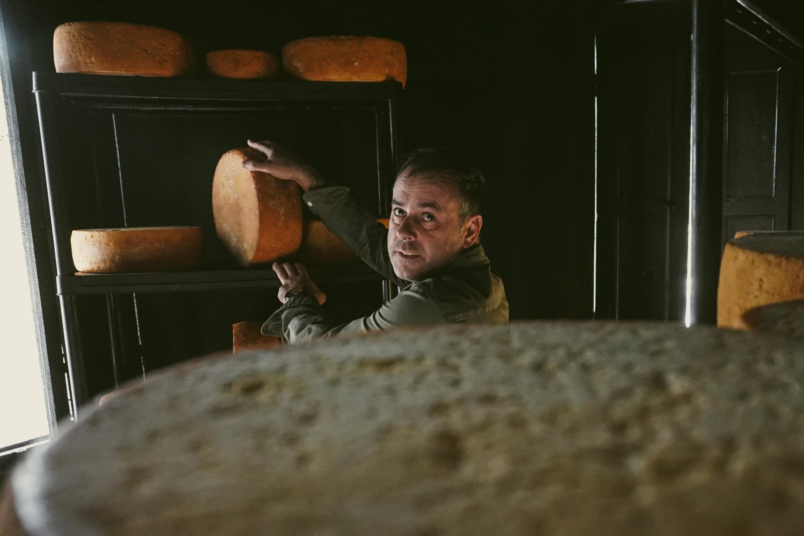 Maestro quesero sosteniendo una rueda de queso en una cámara de maduración